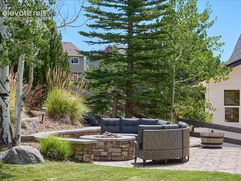 Stone patio with a built-in stone fire pit, tiered landscaping with mature trees, and a retaining wall