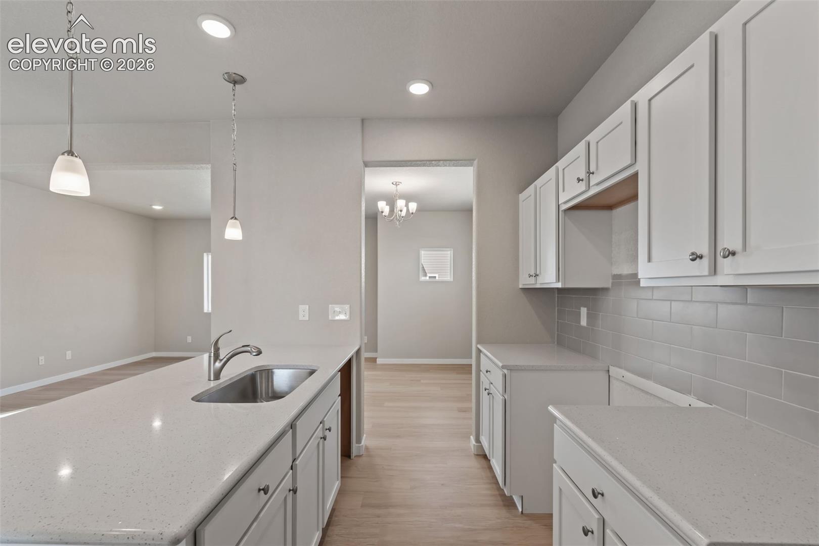 kitchen with white cabinetry, quartz counters, undermount sink in island, and gray subway tile backsplash; chandelier visible in adjacent dining room