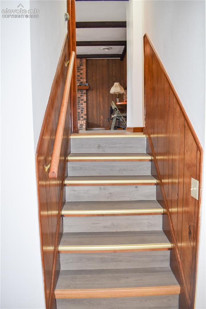 Staircase featuring wood-finish treads with brass-tone nosing, wood paneling, and a wood handrail
