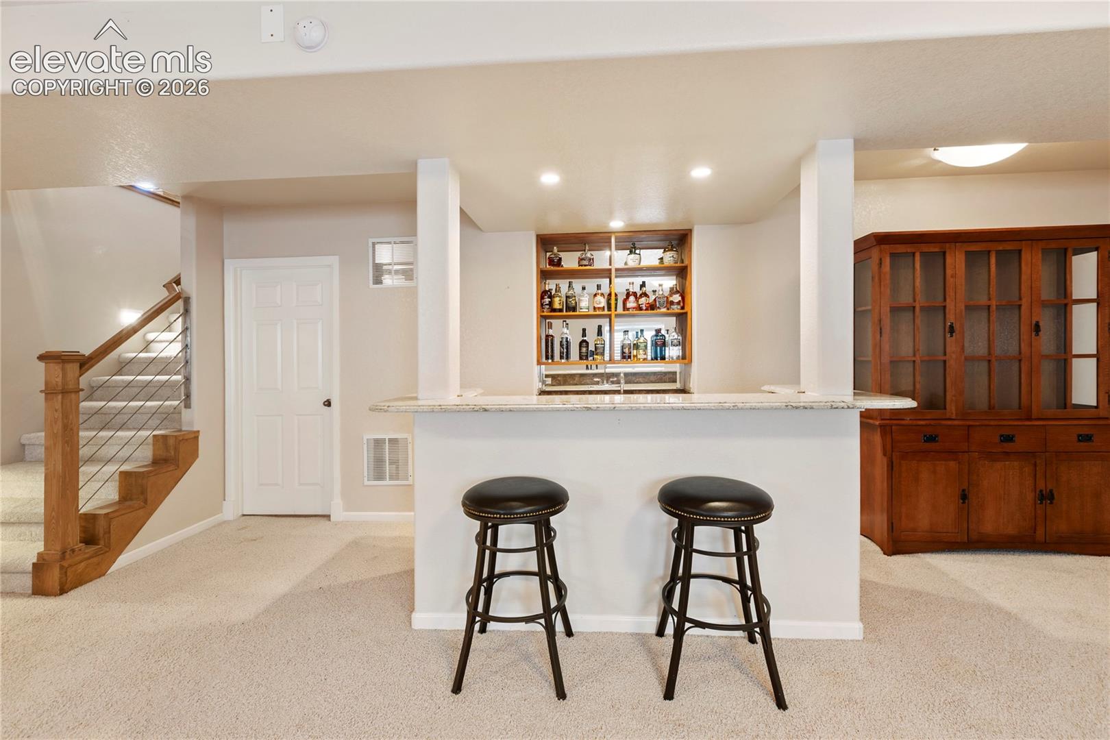 Built-in bar with stone counter, integrated shelving, and recessed lighting