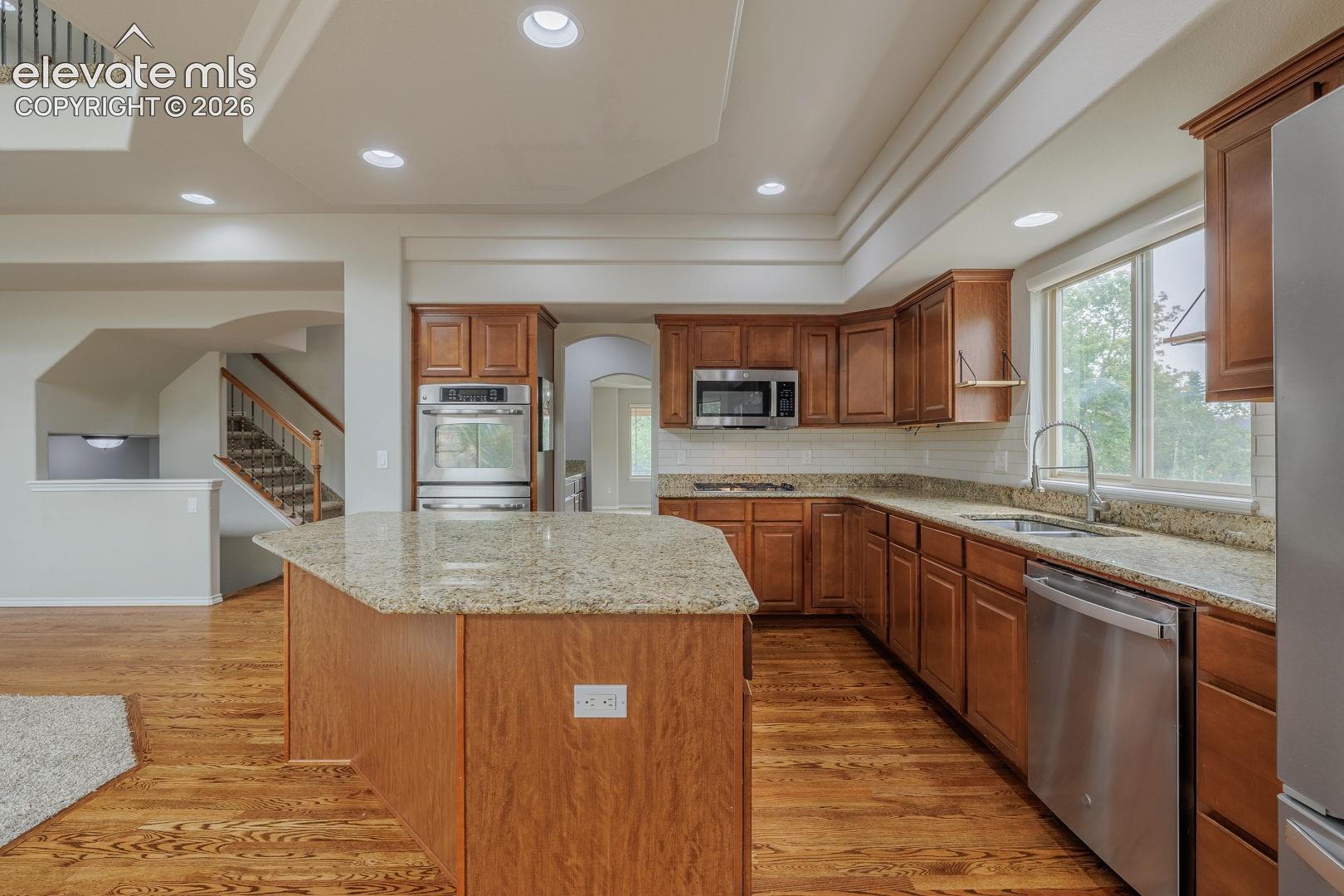 Kitchen featuring wood-finish flooring, a central island with a light-toned countertop, wood cabinetry, stainless steel appliances, and recessed lighting