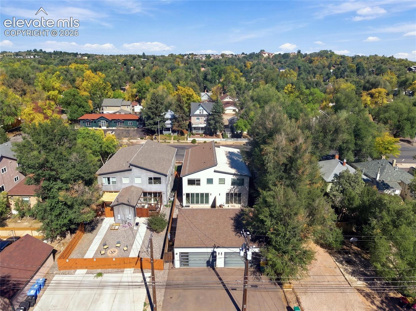 Aerial perspective featuring two multi-level structures with dual-pitched rooflines, integrated two-car garages, and extensive mature tree coverage