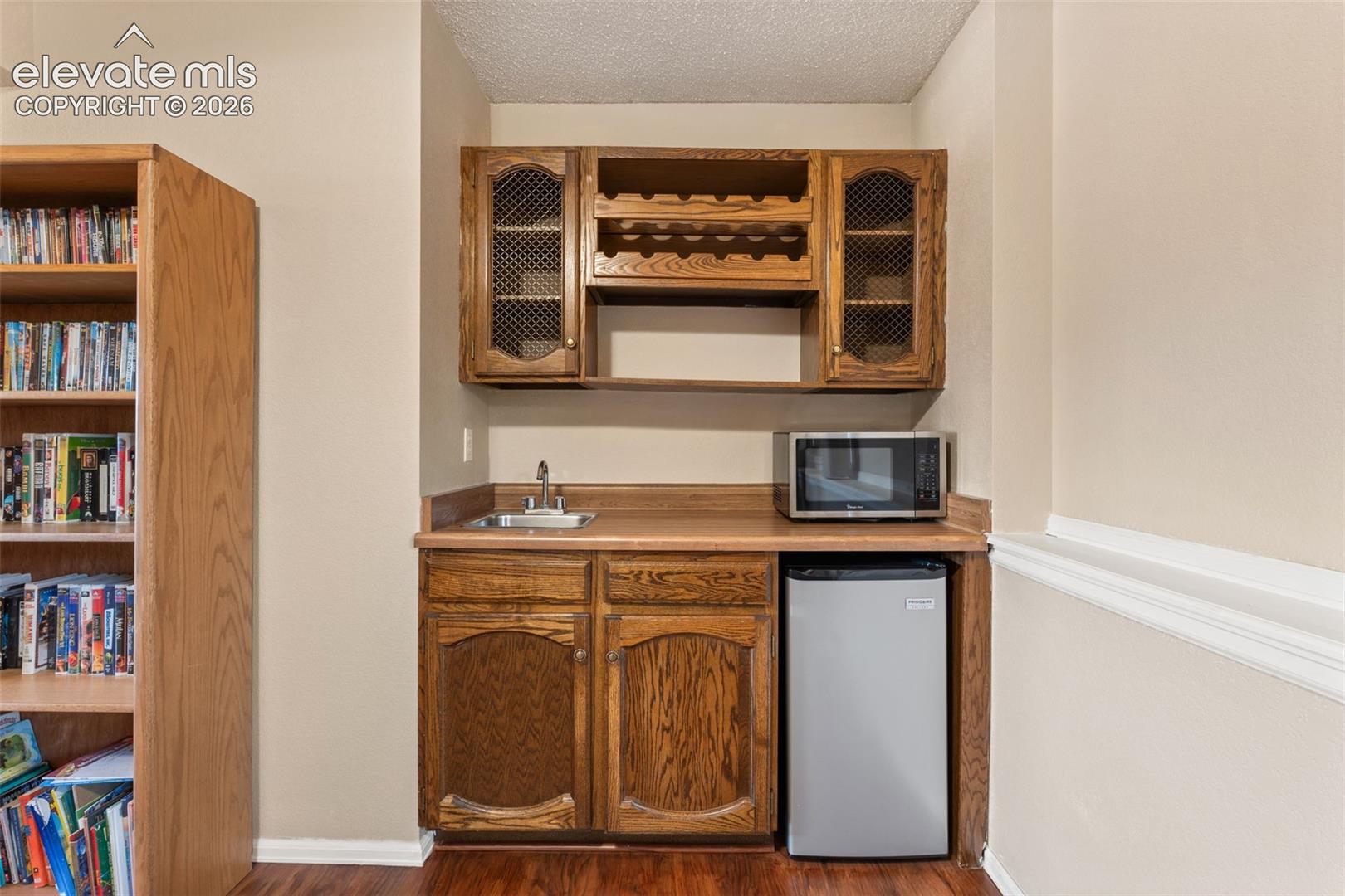 Built-in wood cabinetry featuring upper wire-mesh door fronts, integrated wine rack, recessed sink, and countertop space