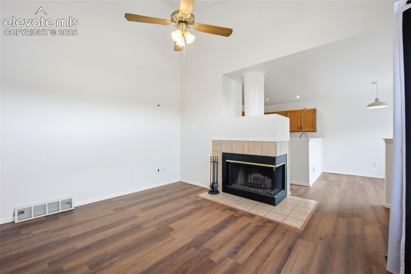Wood-finish flooring, corner fireplace with tile surround, and overhead ceiling fan