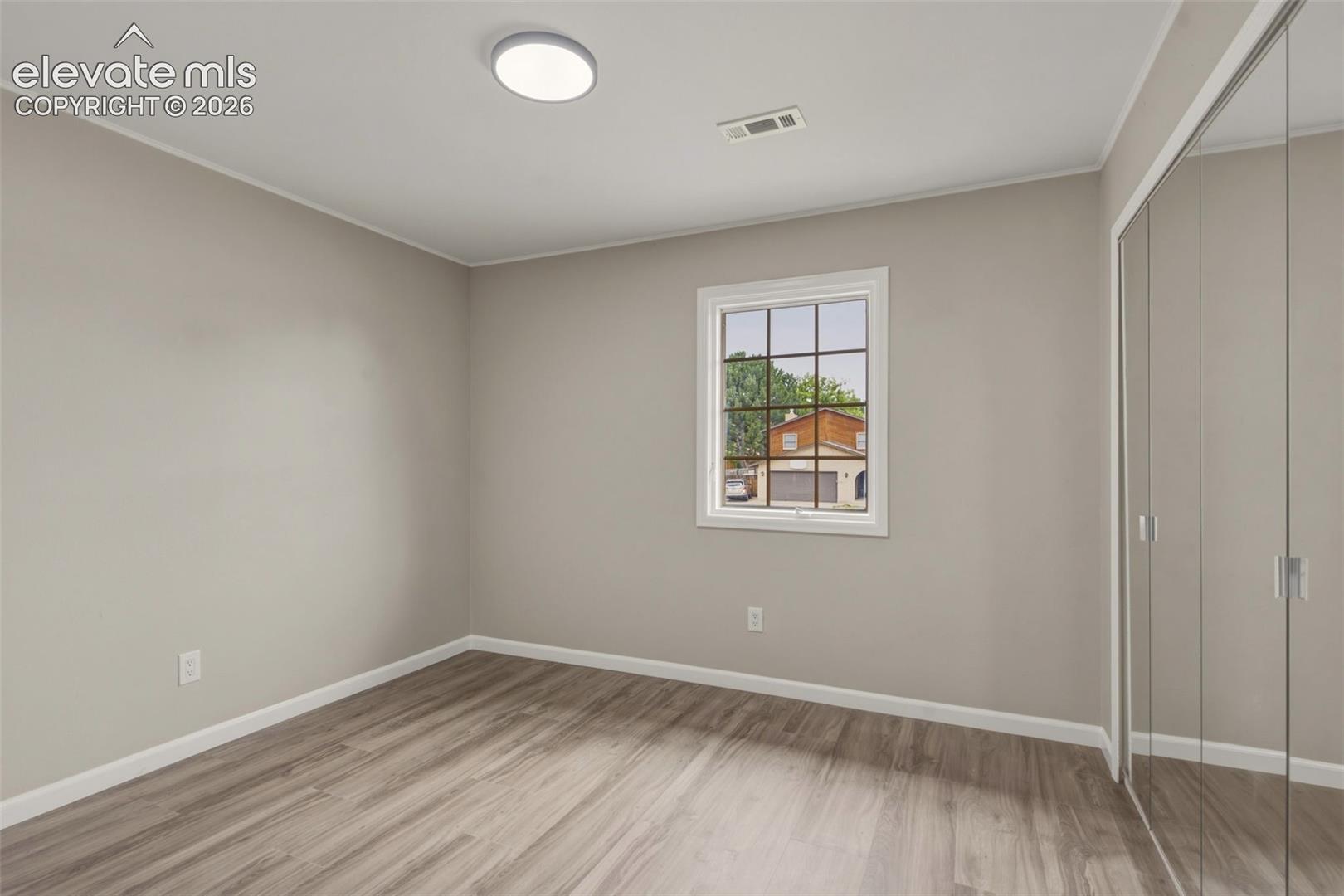 Bright, light-filled bedroom showcasing wood-finish flooring, neutral wall finishes, and abundant natural light from a large multi-pane window