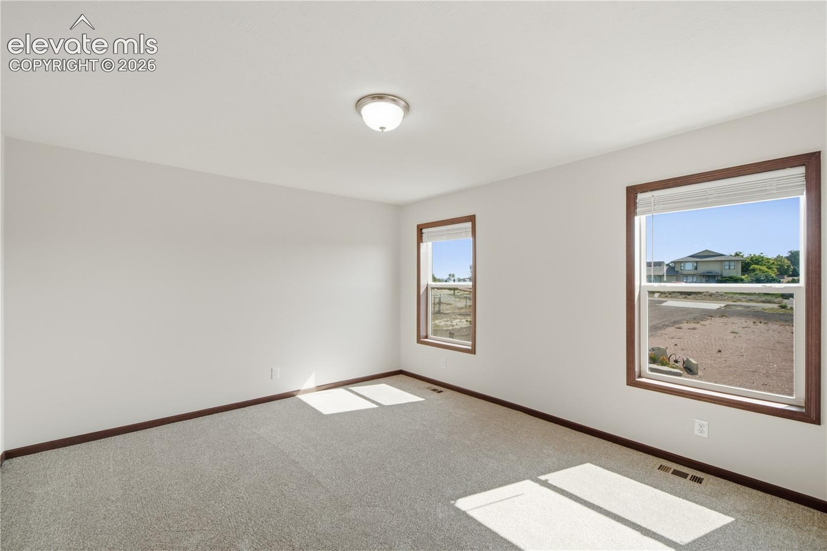 Neutral wall colors, two windows with wood-finish trim, and gray carpeting