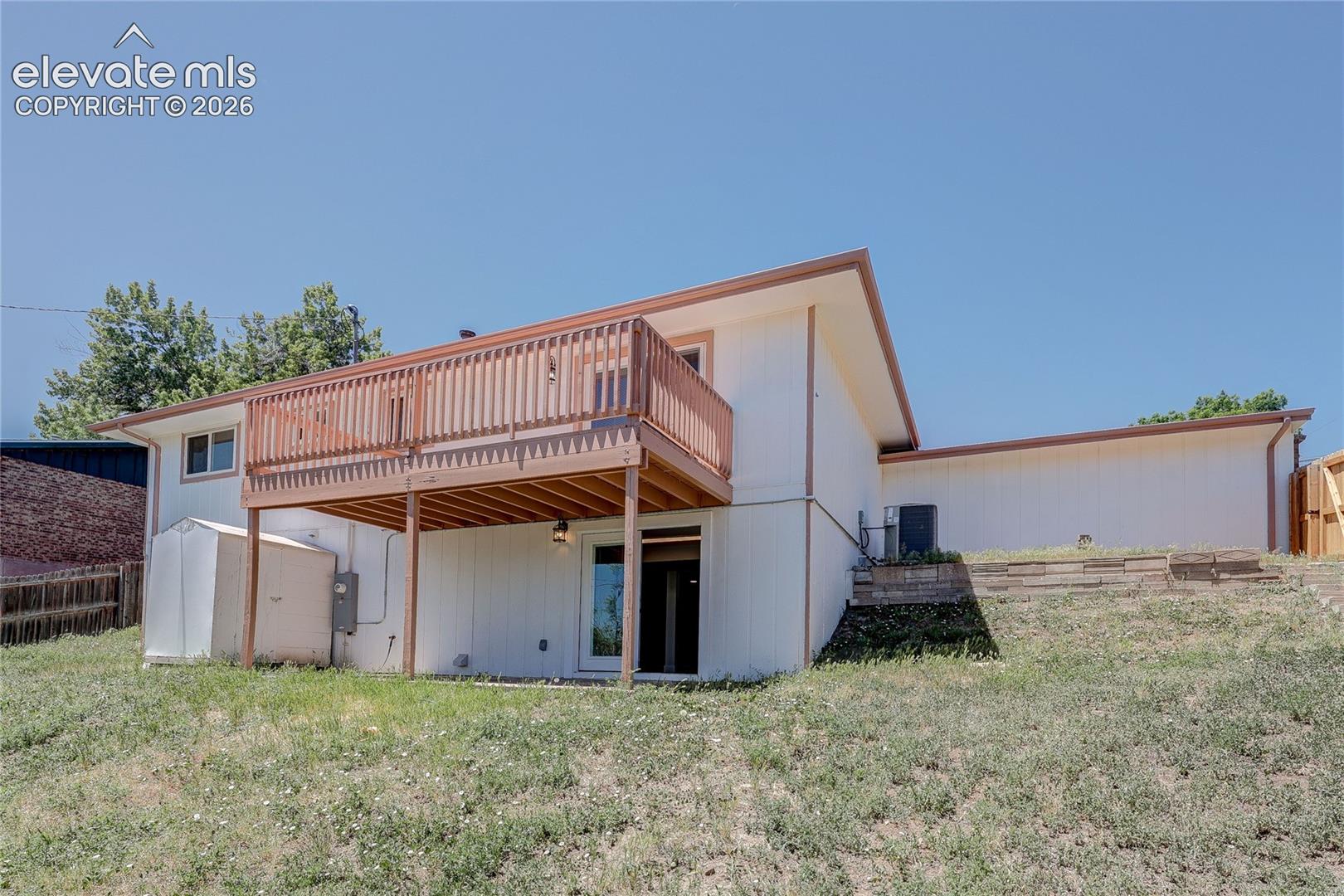 Rear exterior featuring a raised wood deck with vertical balusters, white vertical siding, and a sloped roofline