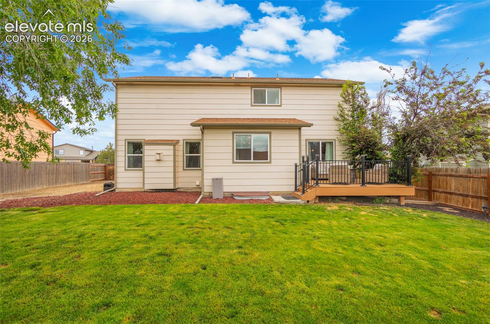 Expansive green lawn with a composite deck, black metal railings, and privacy fencing
