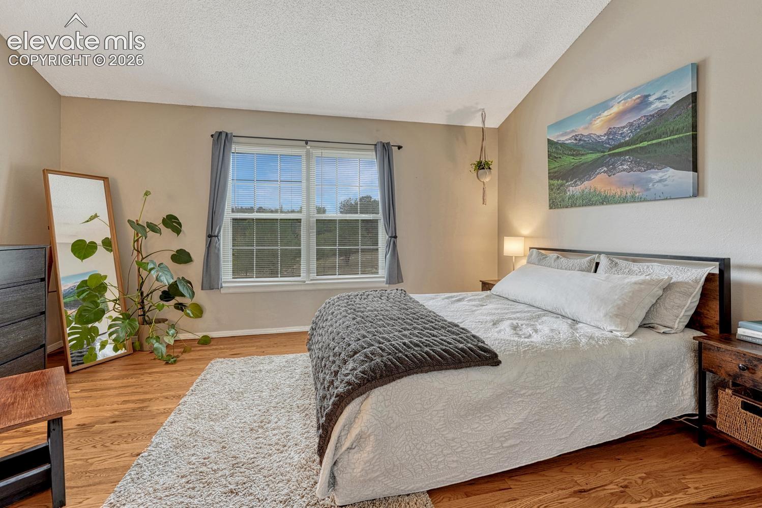 Primary bedroom features harwood floor, vaulted ceiling, and attached bathroom