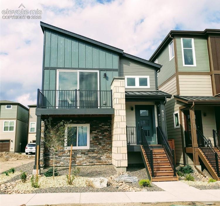 Modern multi-level exterior featuring vertical siding, a stone veneer accent wall, an elevated balcony with black metal railing, and an entry staircase with matching railing