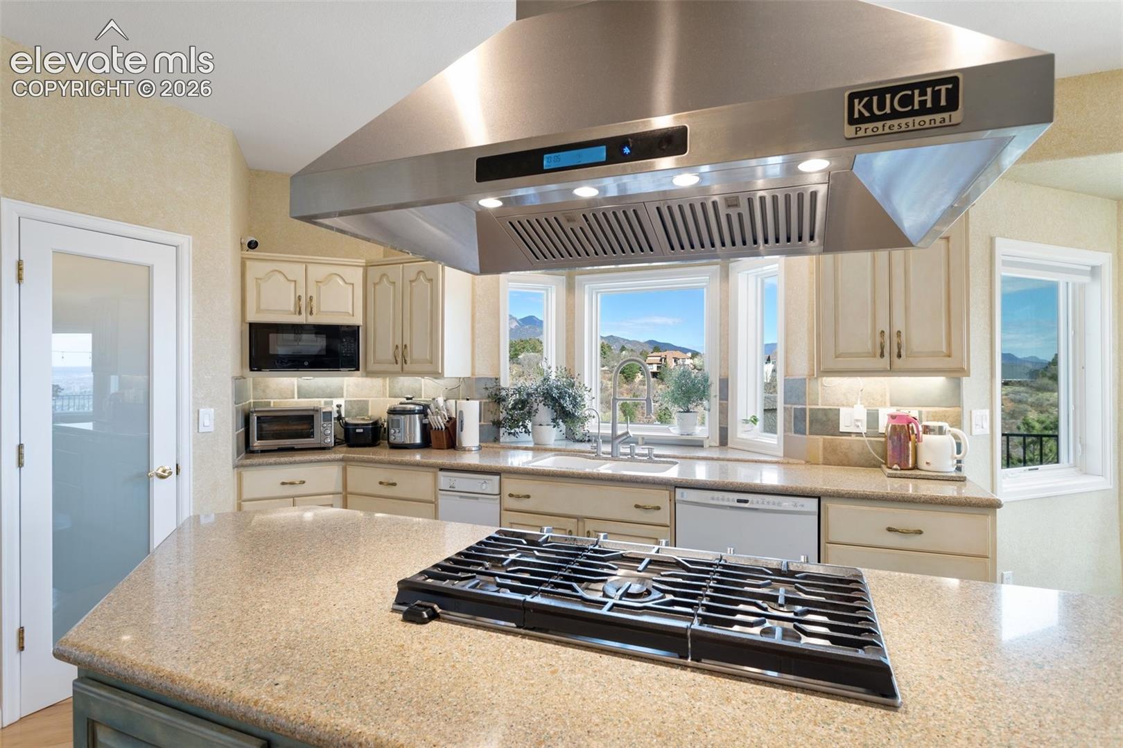 Kitchen featuring a large stainless steel professional range hood, central island with a built-in cooktop, light-toned cabinetry, and a bay window overlooking a mountain landscape