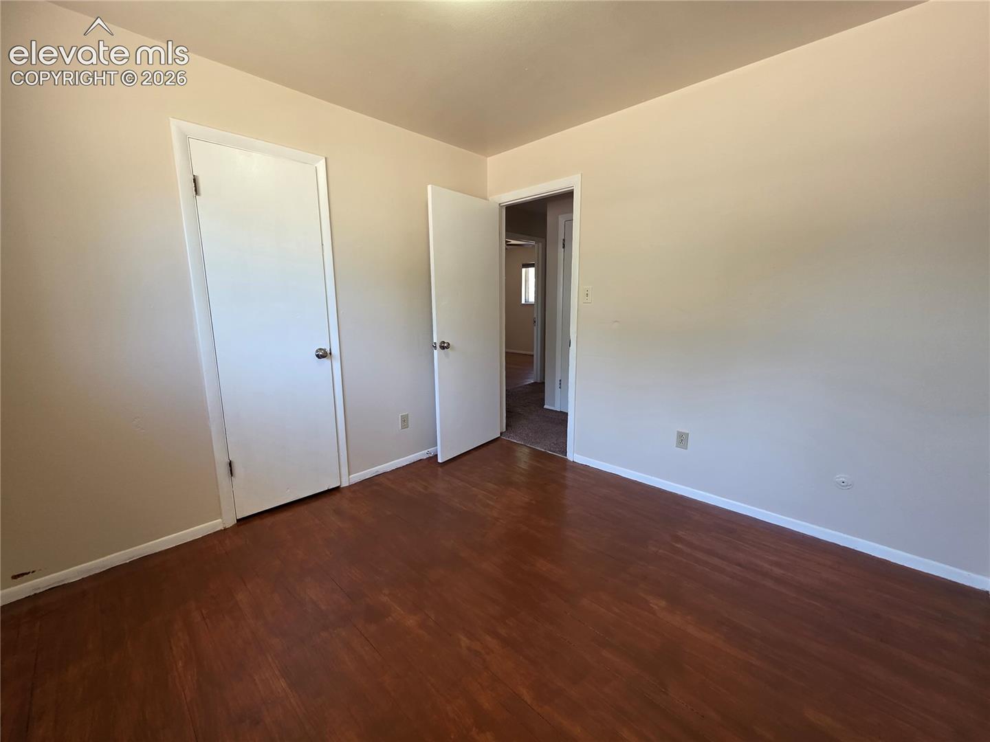 Room featuring wood-finish flooring, light neutral wall tones, white trim, and two white interior doors