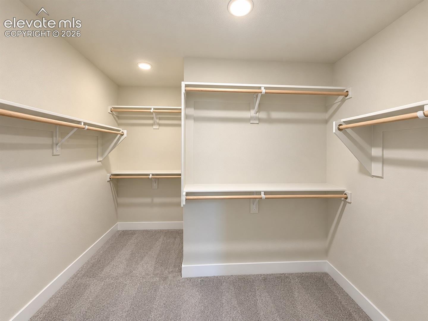 Walk-in closet featuring multi-level wood-finish hanging rods, white shelving, recessed lighting, and wall-to-wall carpeting