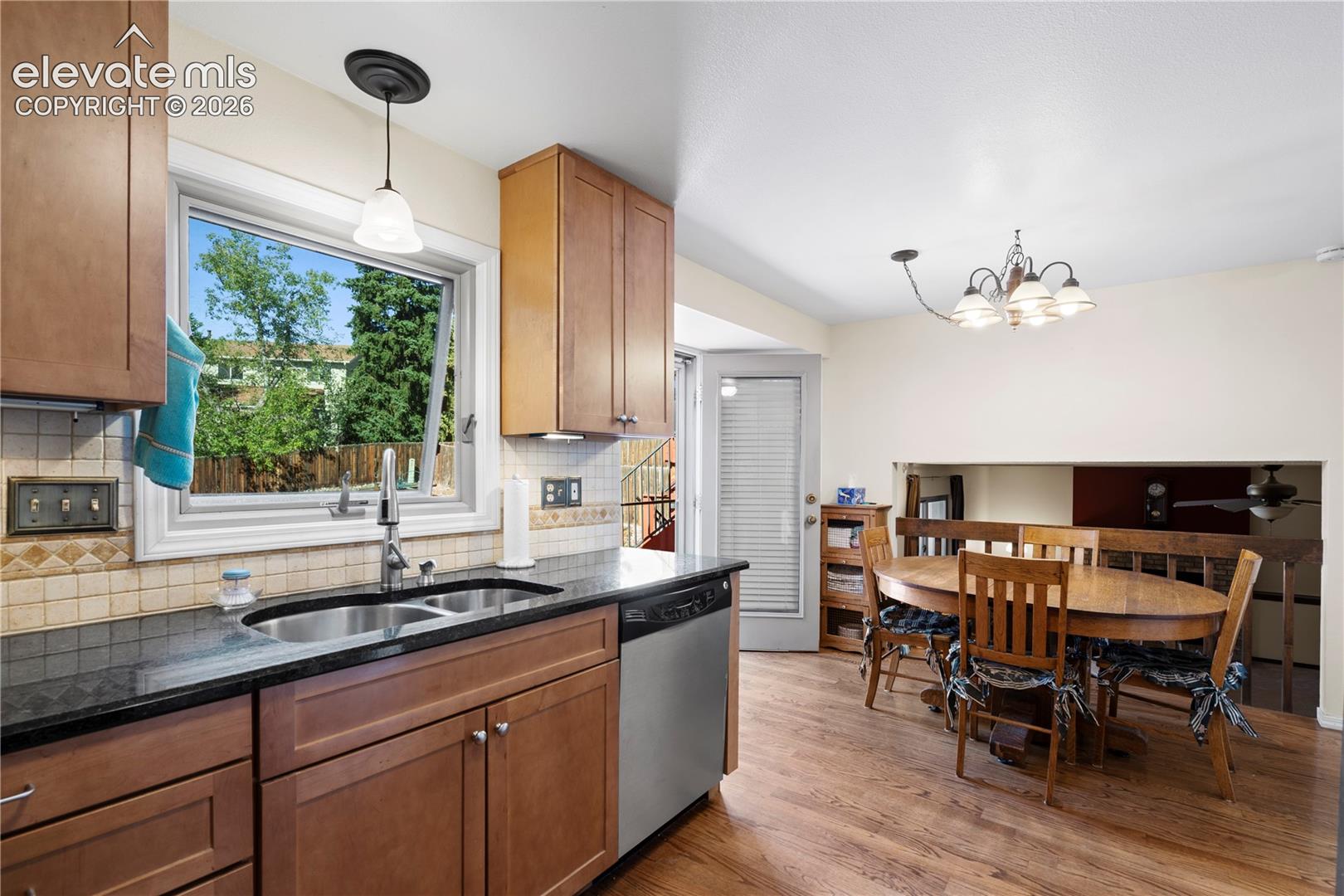 Kitchen featuring wood-finish cabinetry, dark countertops, a double basin sink, and a tiled backsplash