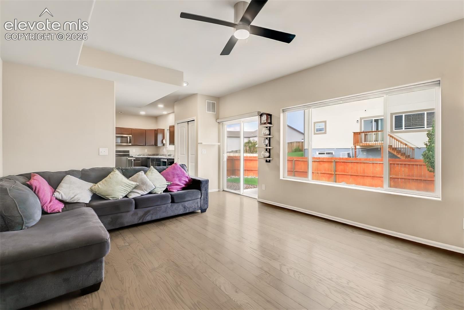 Living area featuring wood-finish flooring, recessed ceiling lighting, a modern ceiling fan, large windows, and a sliding glass door