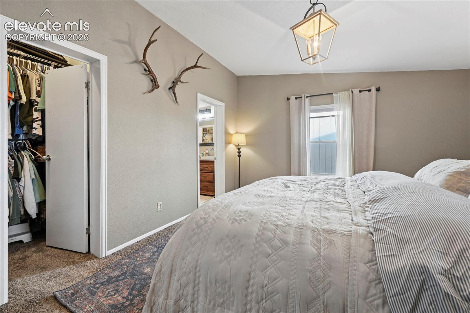 Neutral-toned room featuring a vaulted ceiling, geometric metal lantern pendant light, carpeted flooring, and a walk-in closet