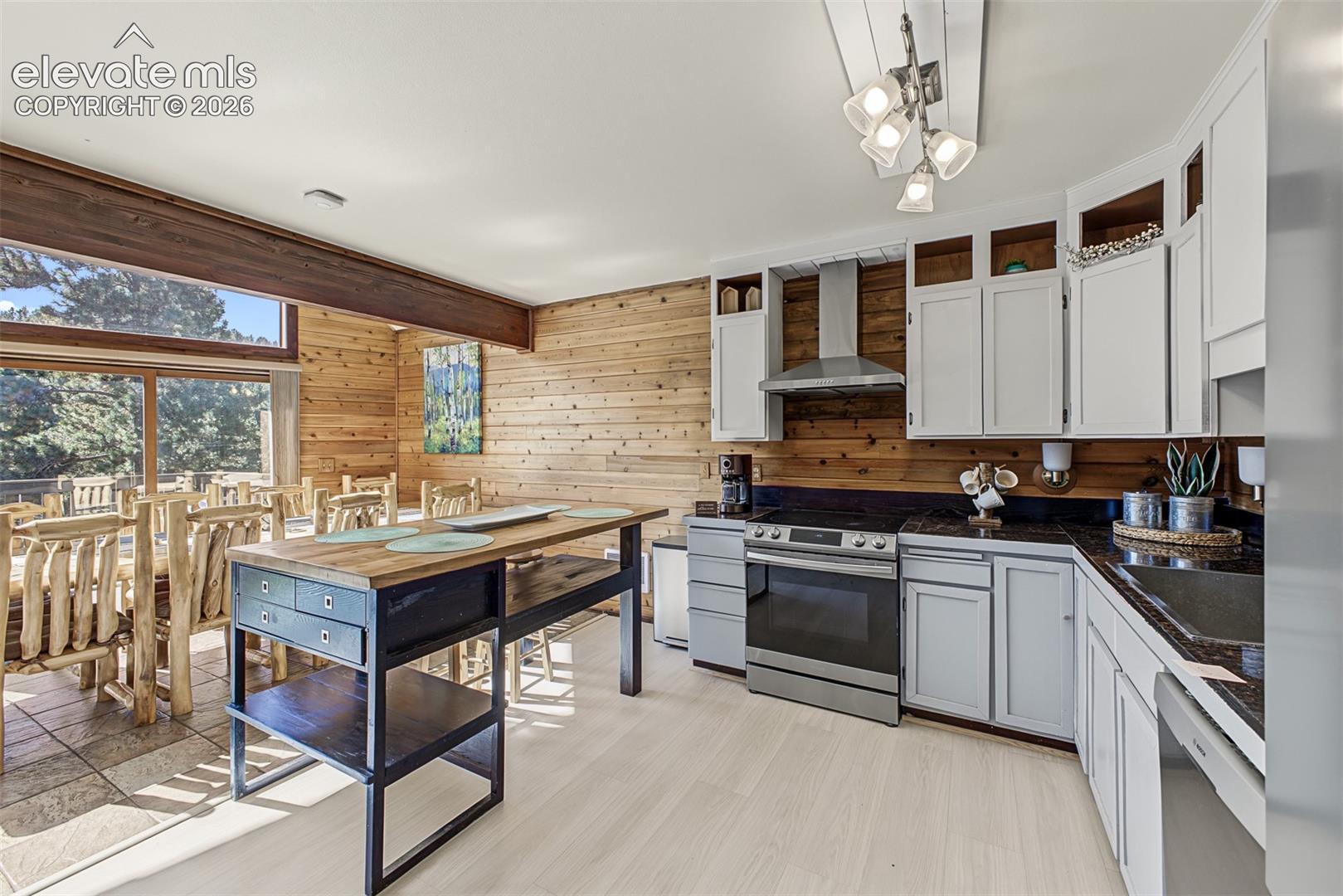 Wood-finish accent wall, built-in stainless steel appliances, white cabinetry, dark countertops, and light wood-finish flooring