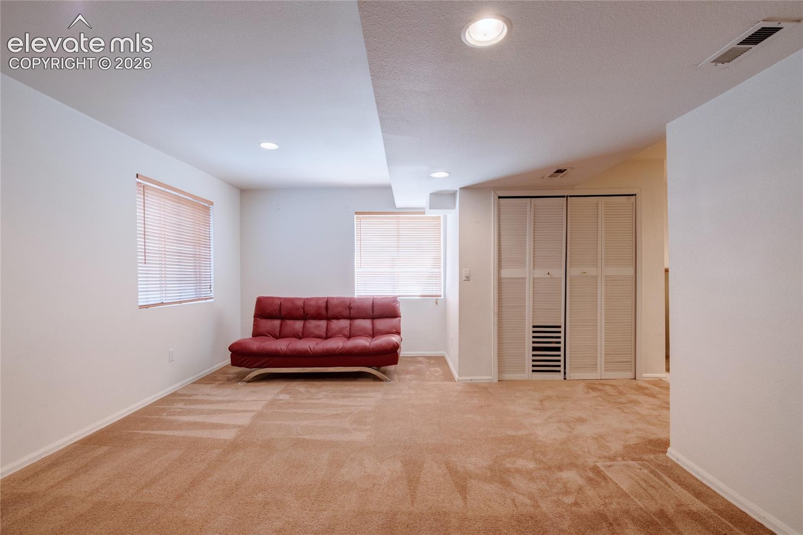 Carpeted room featuring white walls, two windows with horizontal blinds, recessed lighting, and a closet with louvered bi-fold doors