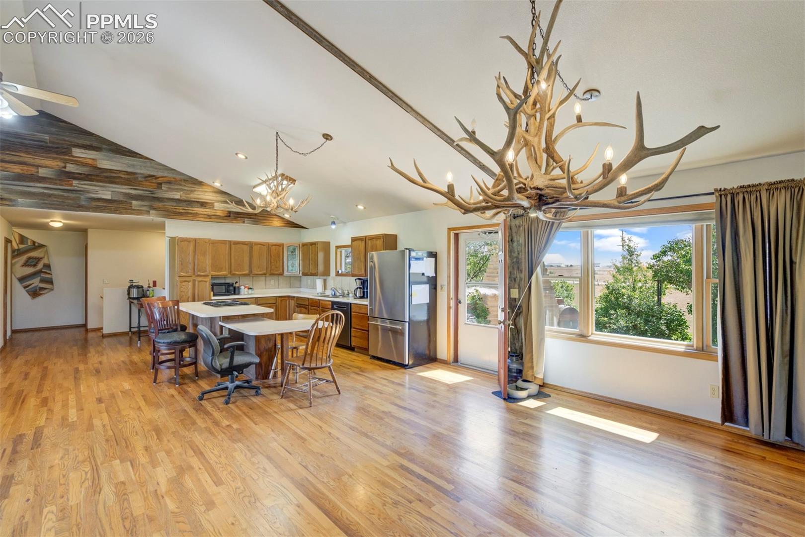 Spacious open-concept living area featuring wood-finish flooring, a vaulted ceiling with exposed wood beams, and a large antler chandelier