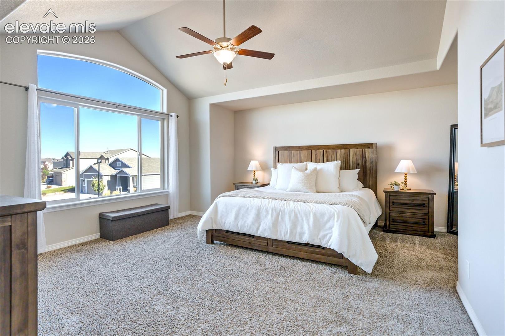 Vaulted ceiling with a ceiling fan, arched window, and plush carpeting