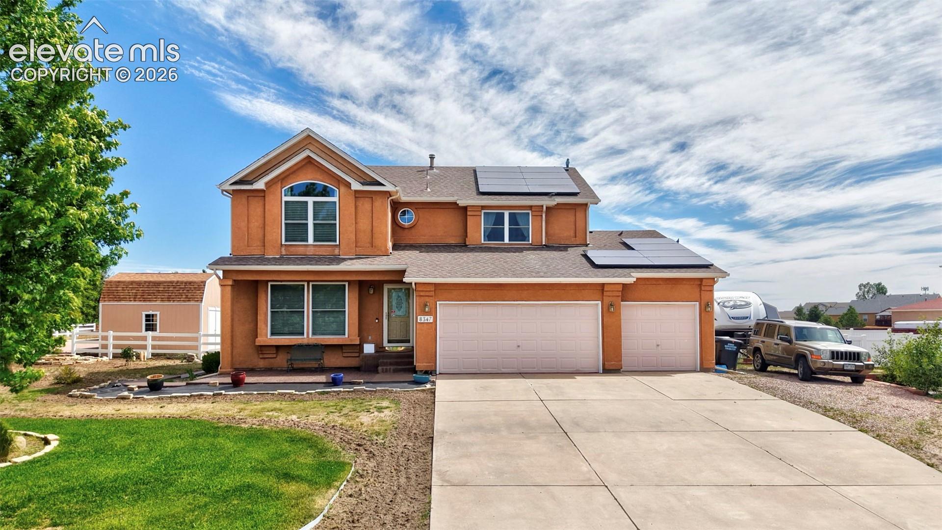 Two-story stucco residence with a concrete driveway, attached two-car garage, and solar panels
