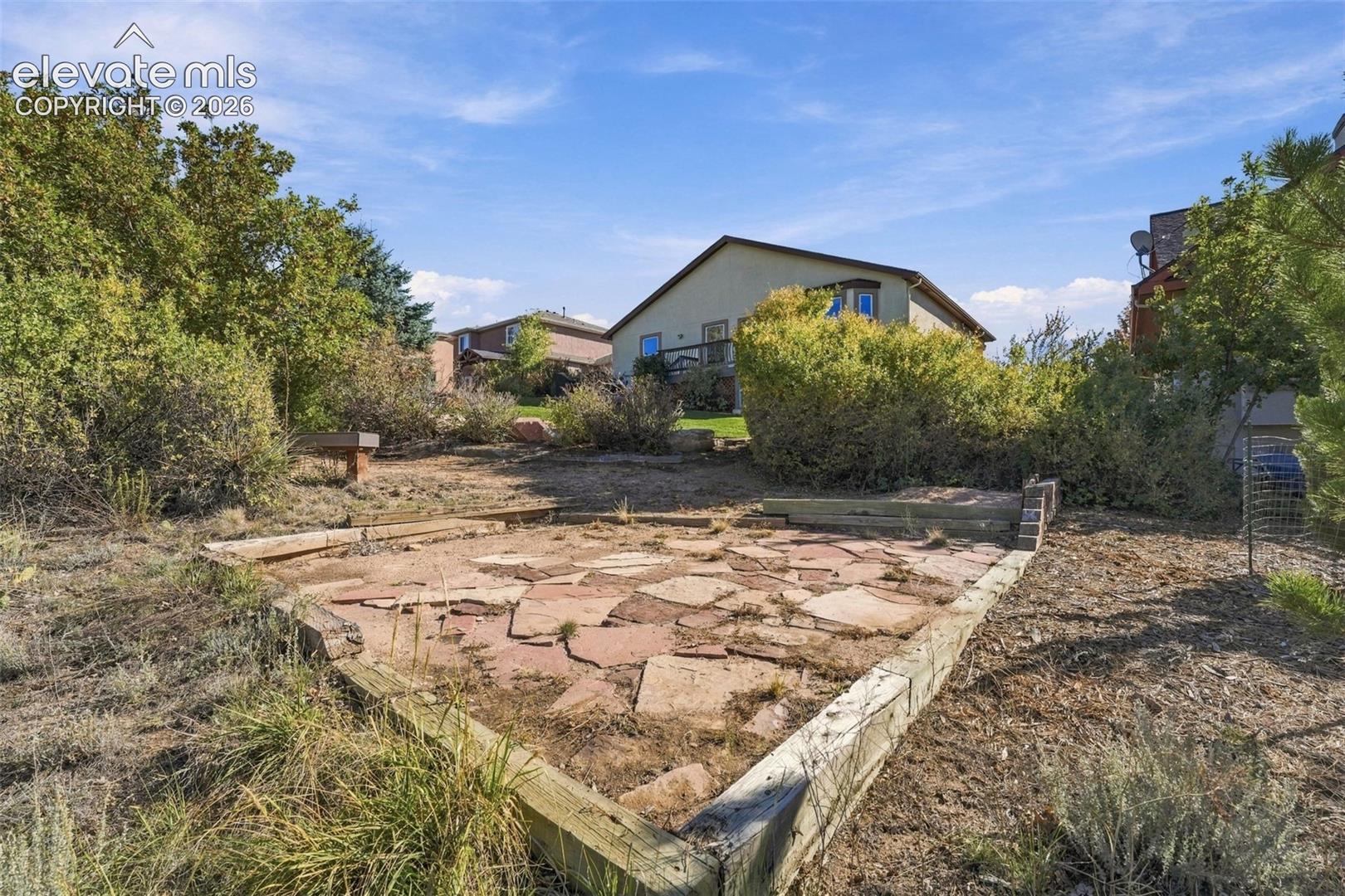 Backyard featuring a tiered stone patio, timber retaining walls, and mature landscaping