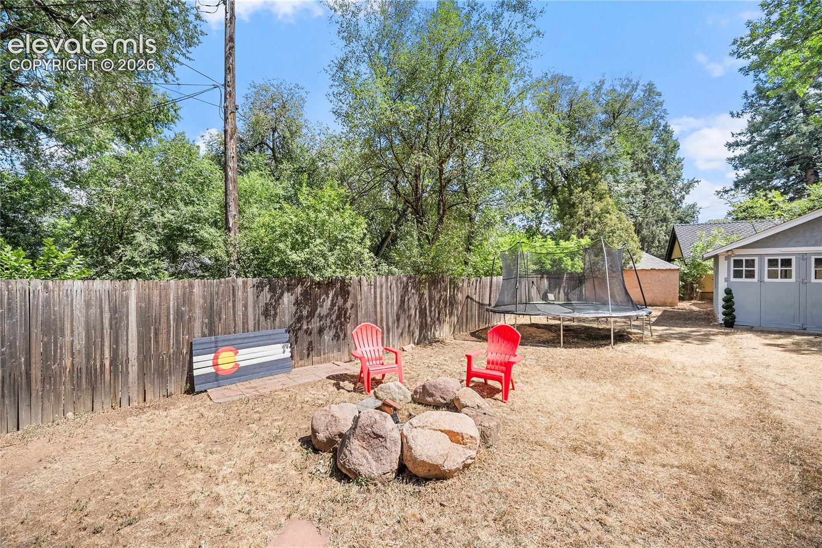 Expansive backyard featuring a natural rock fire pit, wood privacy fencing, a gray exterior garage, and mature perimeter trees