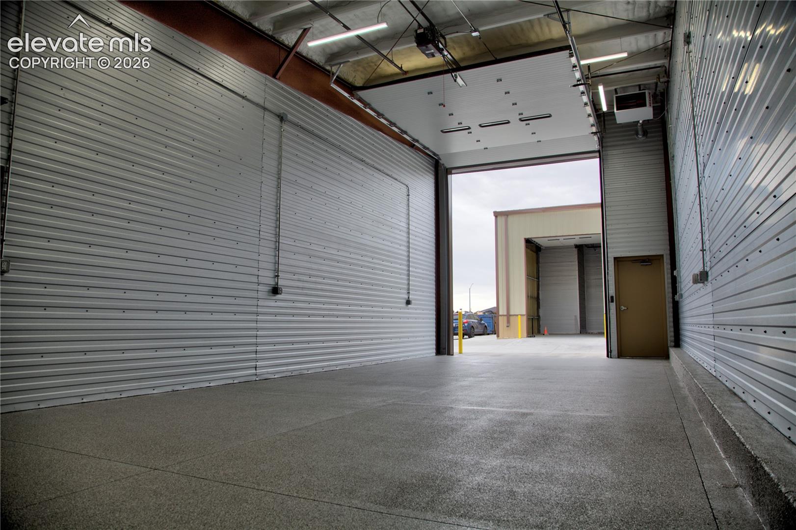 Expansive commercial space featuring high ceilings, multiple overhead doors, durable concrete flooring, and corrugated metal walls