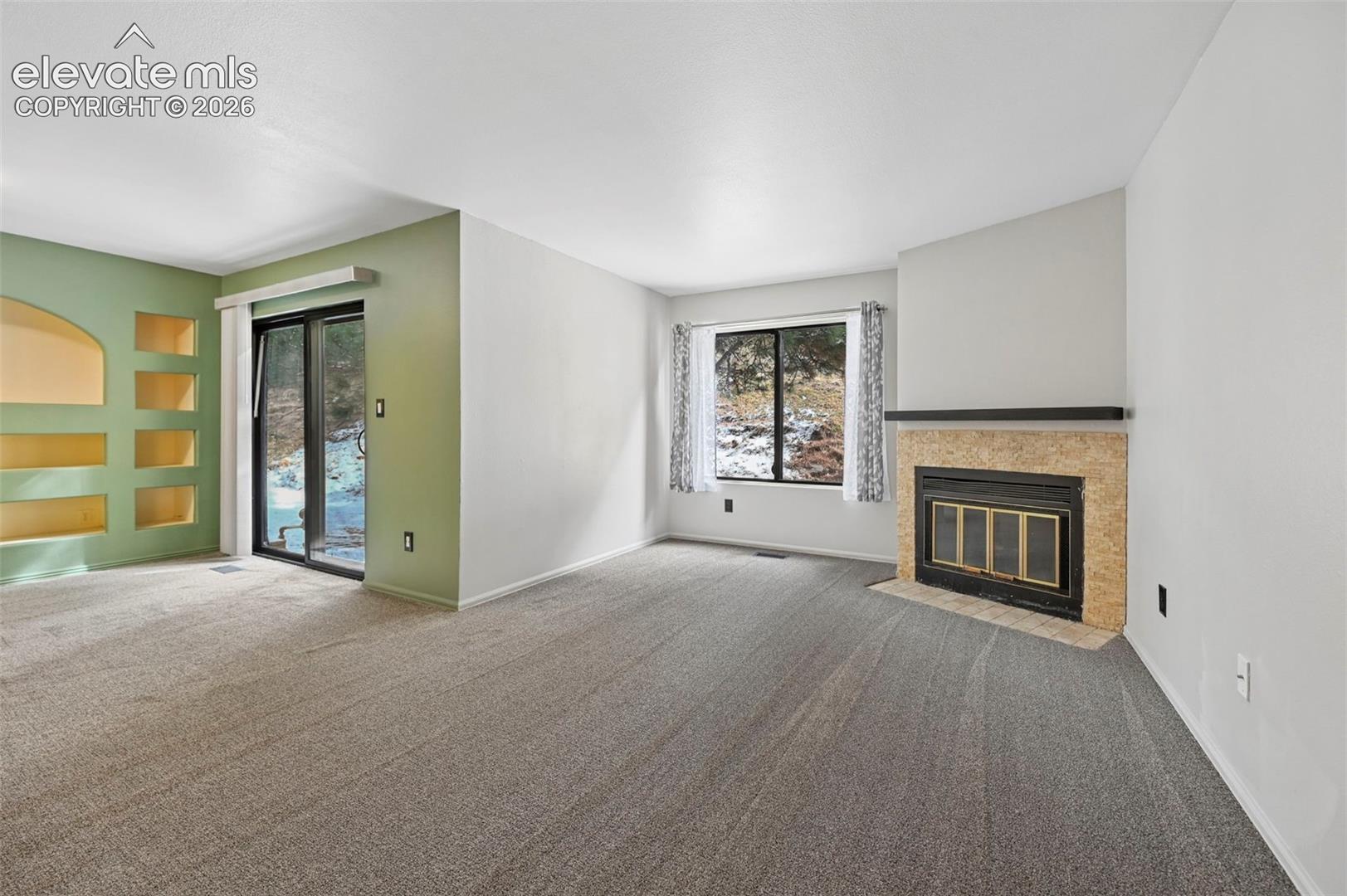 Carpeted room featuring a stone-clad fireplace with metal insert, built-in wall niches, and a sliding glass door to the exterior