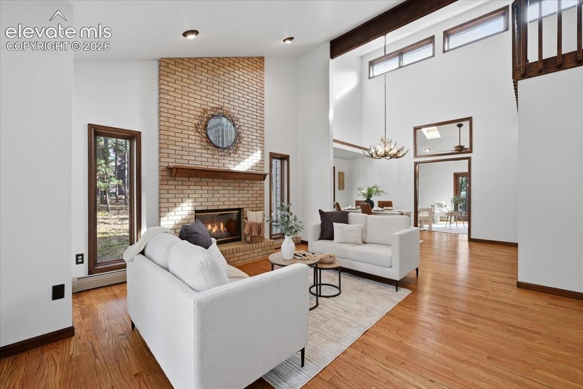 Vaulted ceilings with exposed beams, brick-faced fireplace with wood mantel, hardwood flooring, recessed lighting, and large windows with dark wood trim