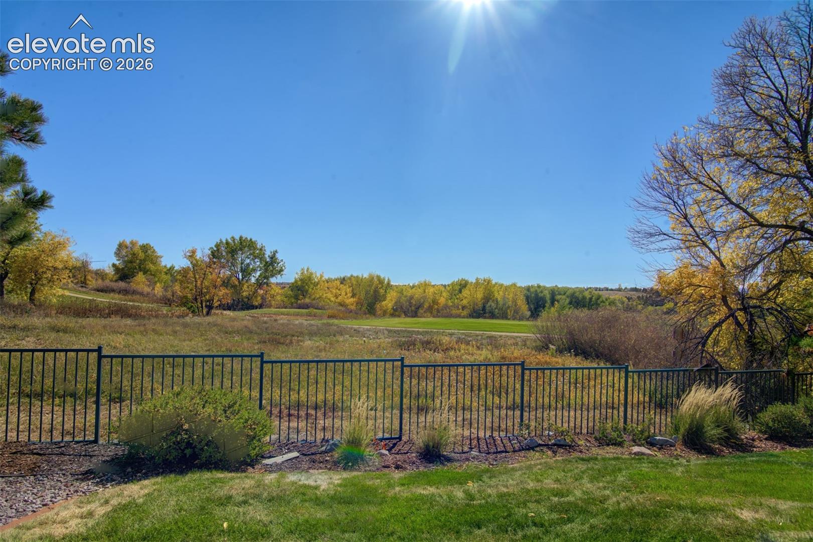 Expansive lot featuring a metal picket fence, manicured grass, and natural landscape borders