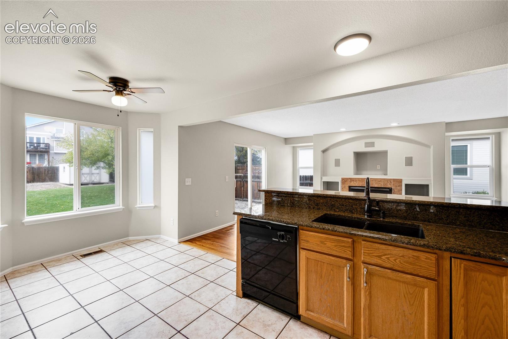 Kitchen featuring wood cabinetry, stone-finish countertops, black appliances, tile flooring, and a bay window