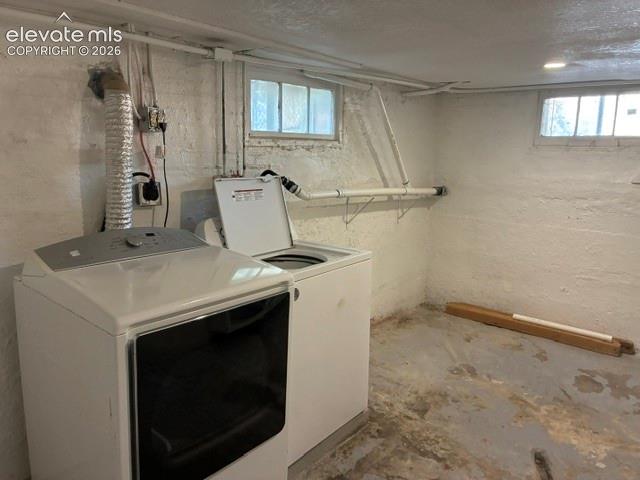 Laundry area featuring a concrete floor, two windows, and exposed ceiling pipes