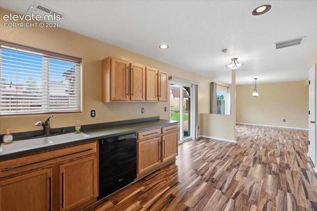 Warm wood-finish flooring throughout, light wood cabinetry, recessed lighting, and a sliding glass door providing access to the outdoors