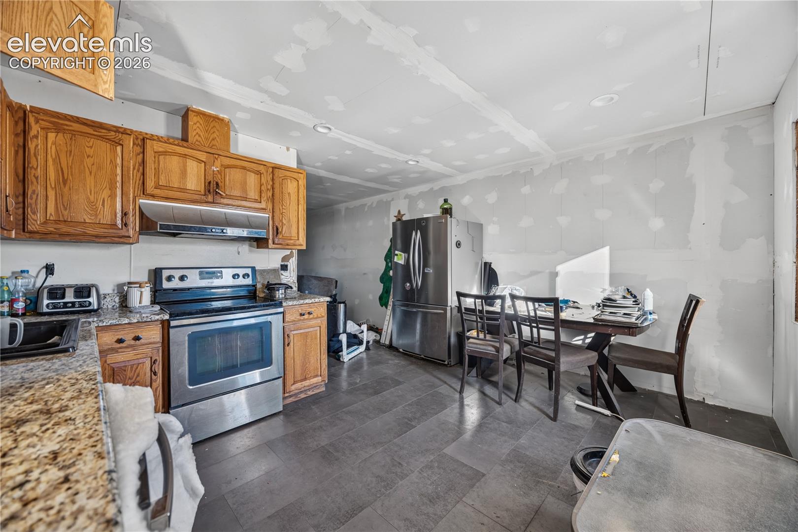 Kitchen featuring natural wood cabinetry, stone-patterned countertops, stainless steel appliances, and tile flooring