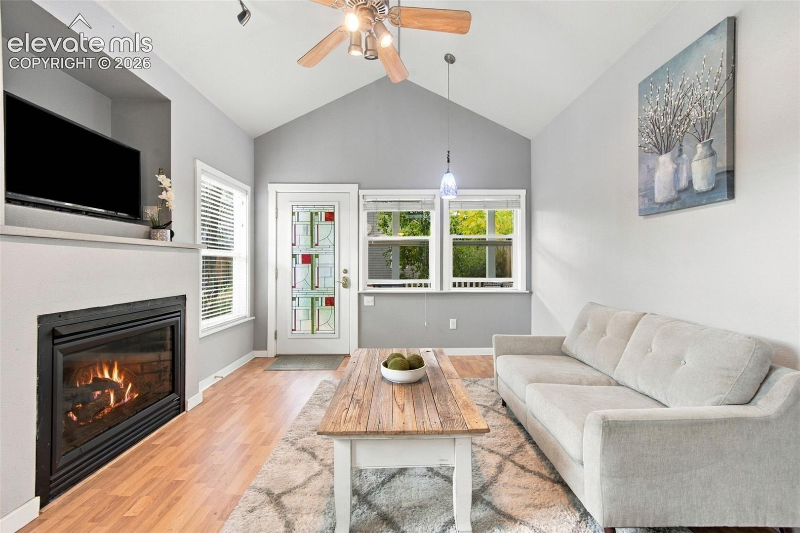 Vaulted ceiling, built-in fireplace with recessed television alcove, wood-finish flooring, and glass-paneled exterior door