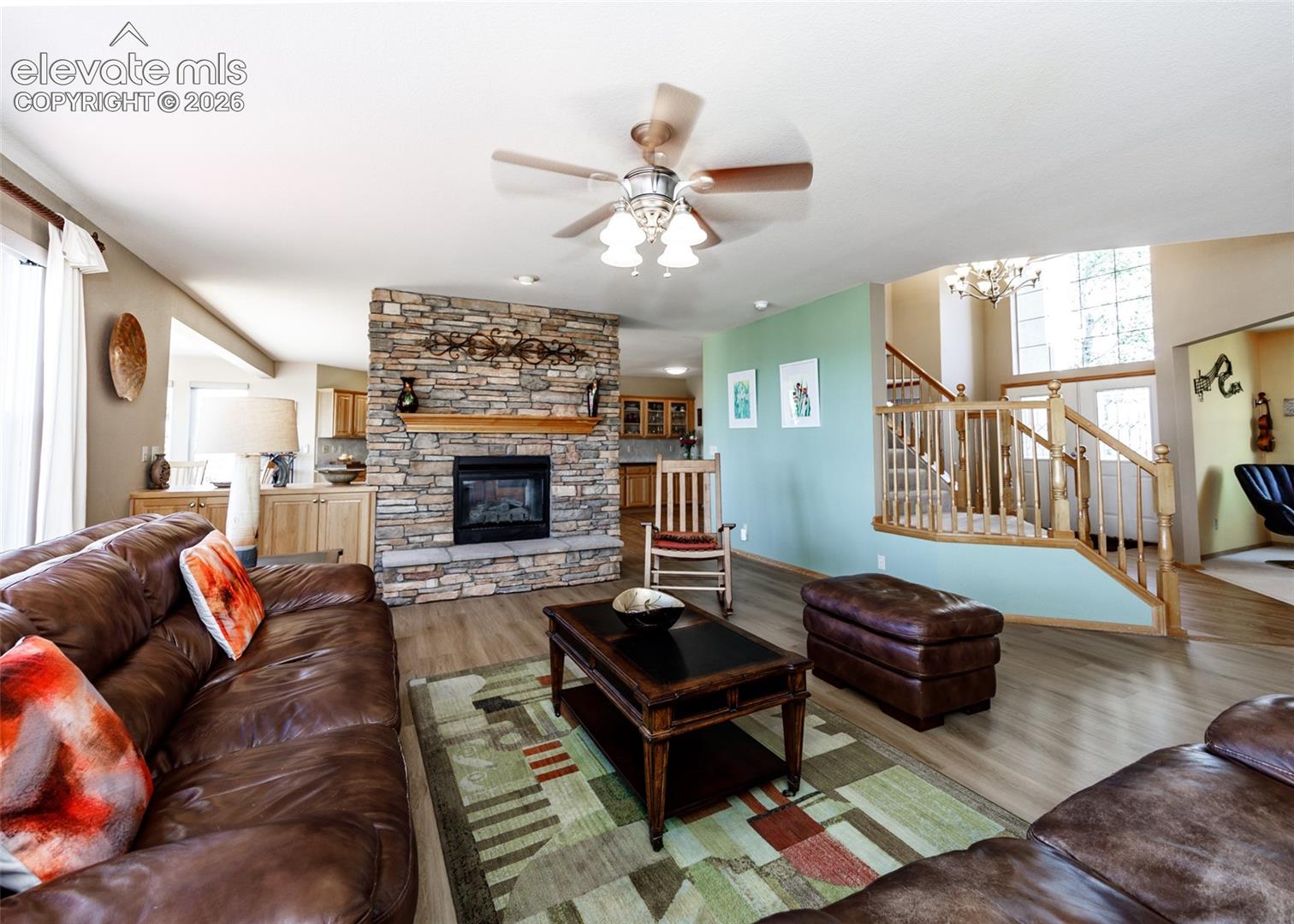 Spacious living area featuring a stone-clad fireplace with a wood mantel, wood-finish flooring, and a multi-level staircase with wood banisters