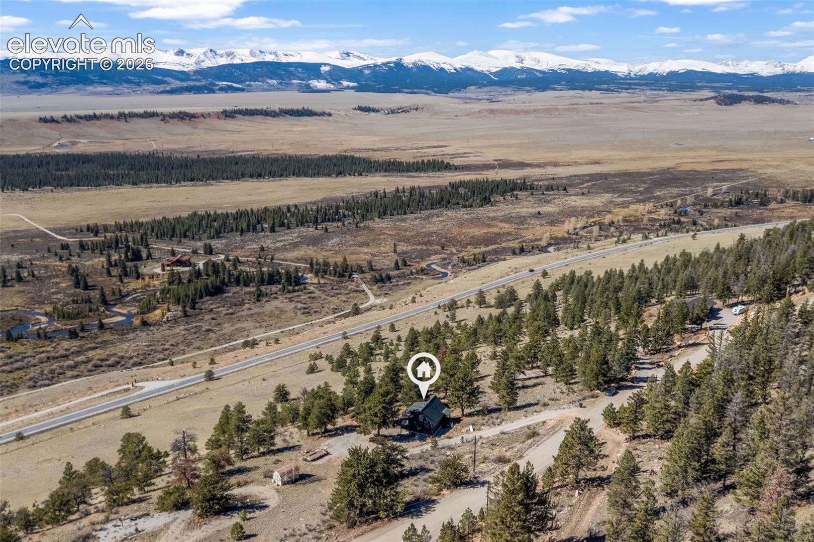 Aerial perspective featuring a timber-sided residence nestled within a forested landscape, accented by expansive mountain range scenery
