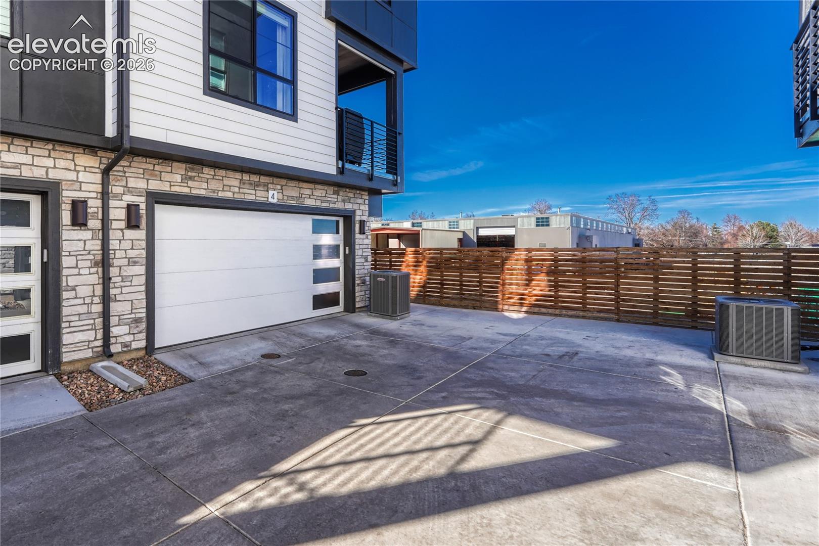 Exterior featuring a stone veneer facade, horizontal lap siding, a metal-accented garage door with glass panel inserts, and a horizontal wood privacy fence