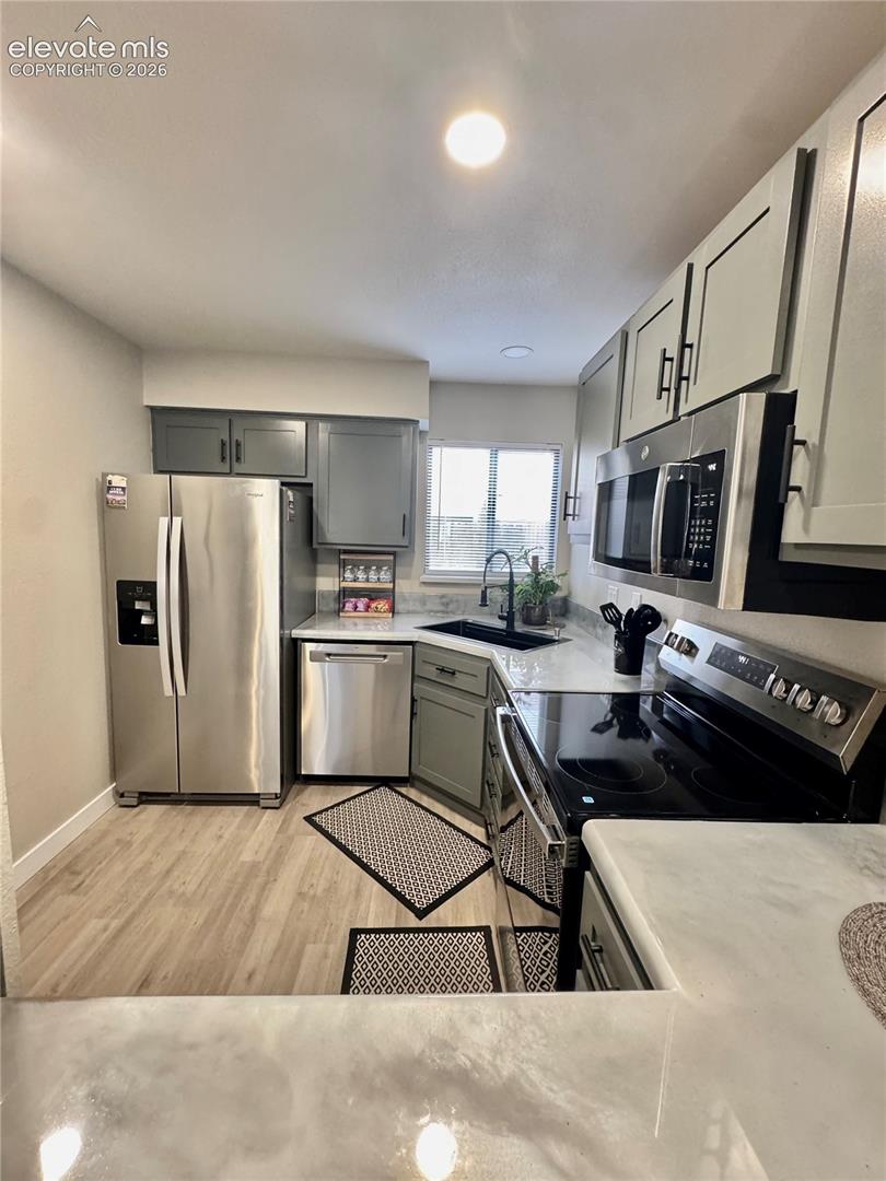 Kitchen featuring stainless steel appliances, light-toned cabinetry, solid surface countertops, a black undermount sink with a pull-down faucet, and wood-finish flooring