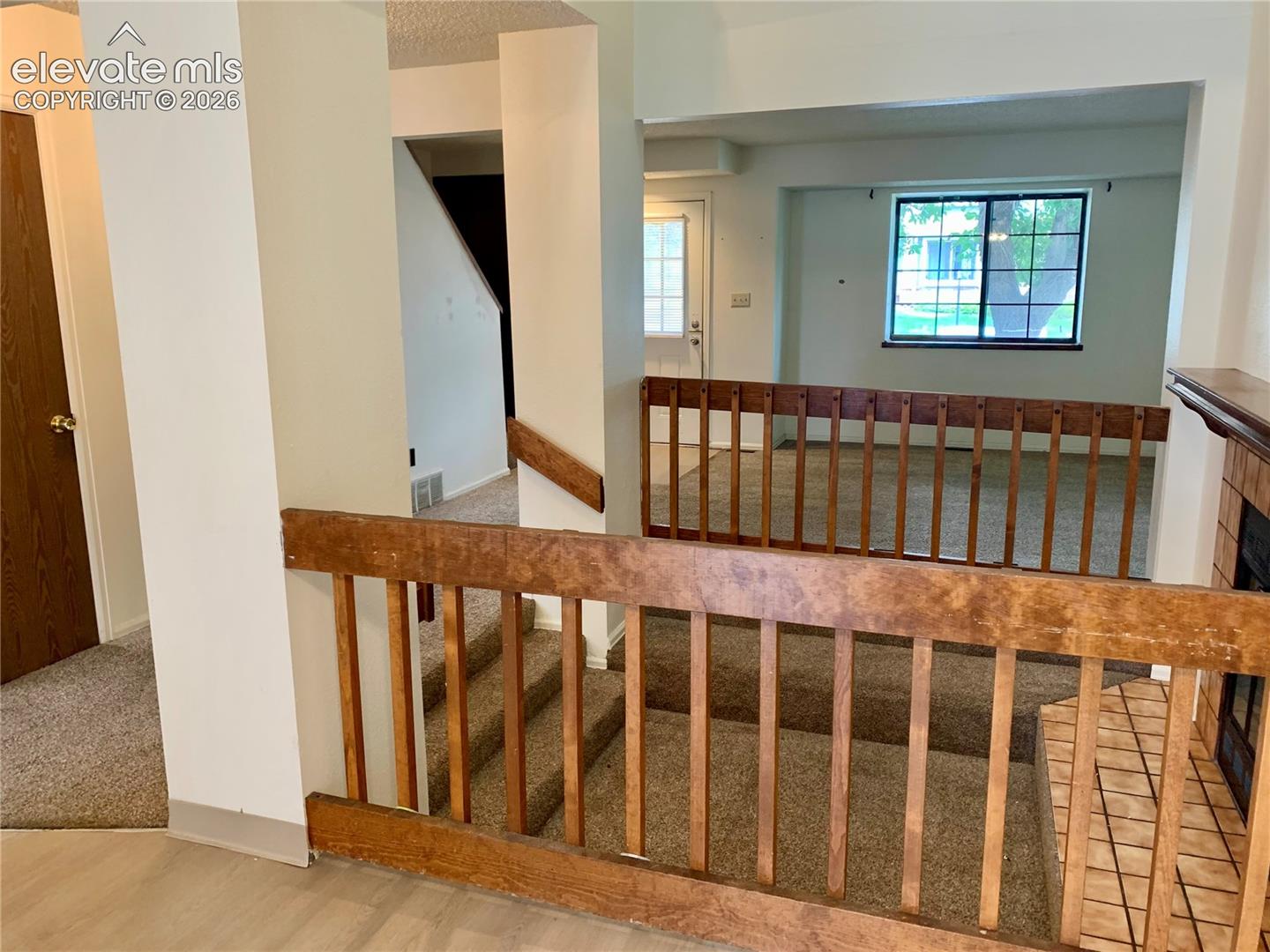 Dining room with view into living room areas featuring wood-finish railings, and a tiled fireplace surround