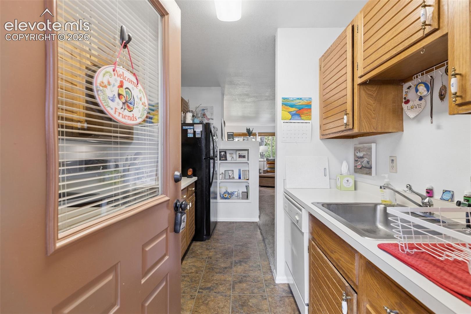 Galley kitchen featuring wood-finish cabinetry, solid surface countertops, a stainless steel sink, and a built-in dishwasher