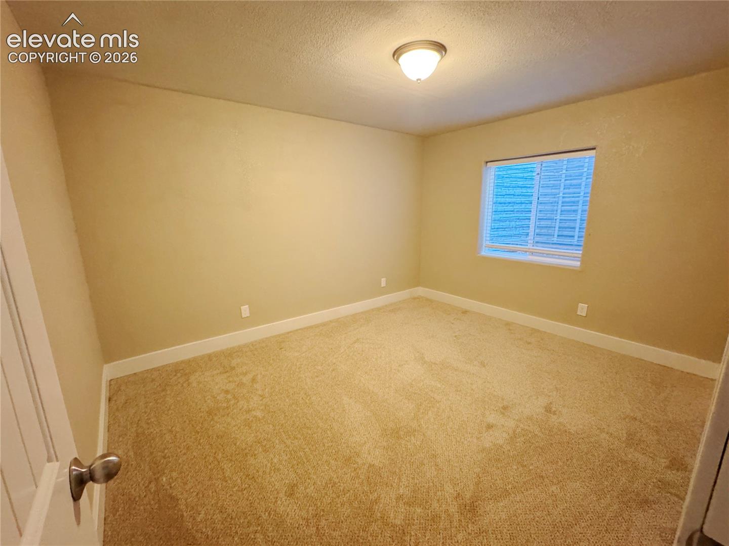 Neutral-toned carpeted room featuring a single window and a central flush-mount ceiling light fixture