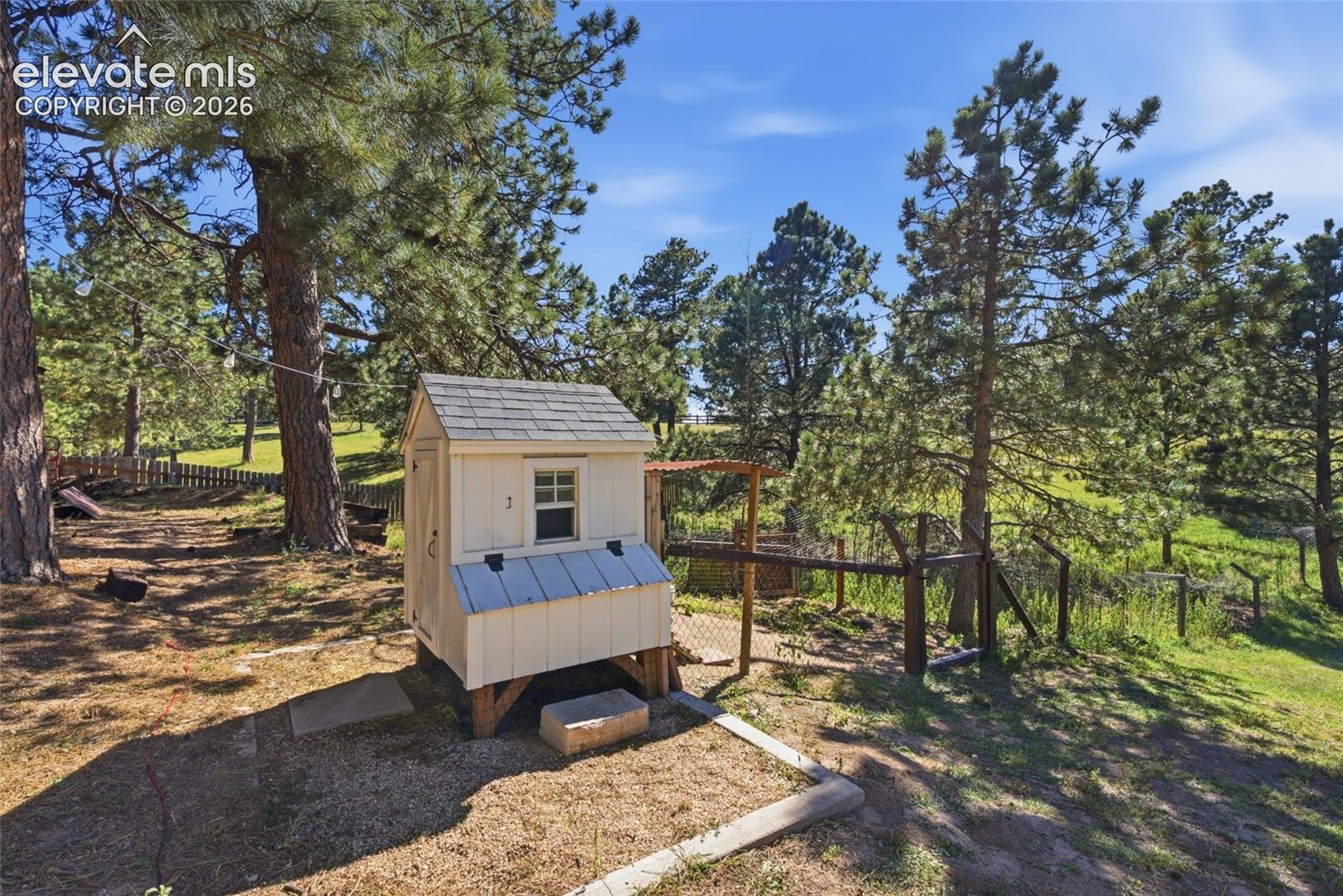 Fenced enclosure with a chicken coop, surrounded by mature trees and natural landscaping