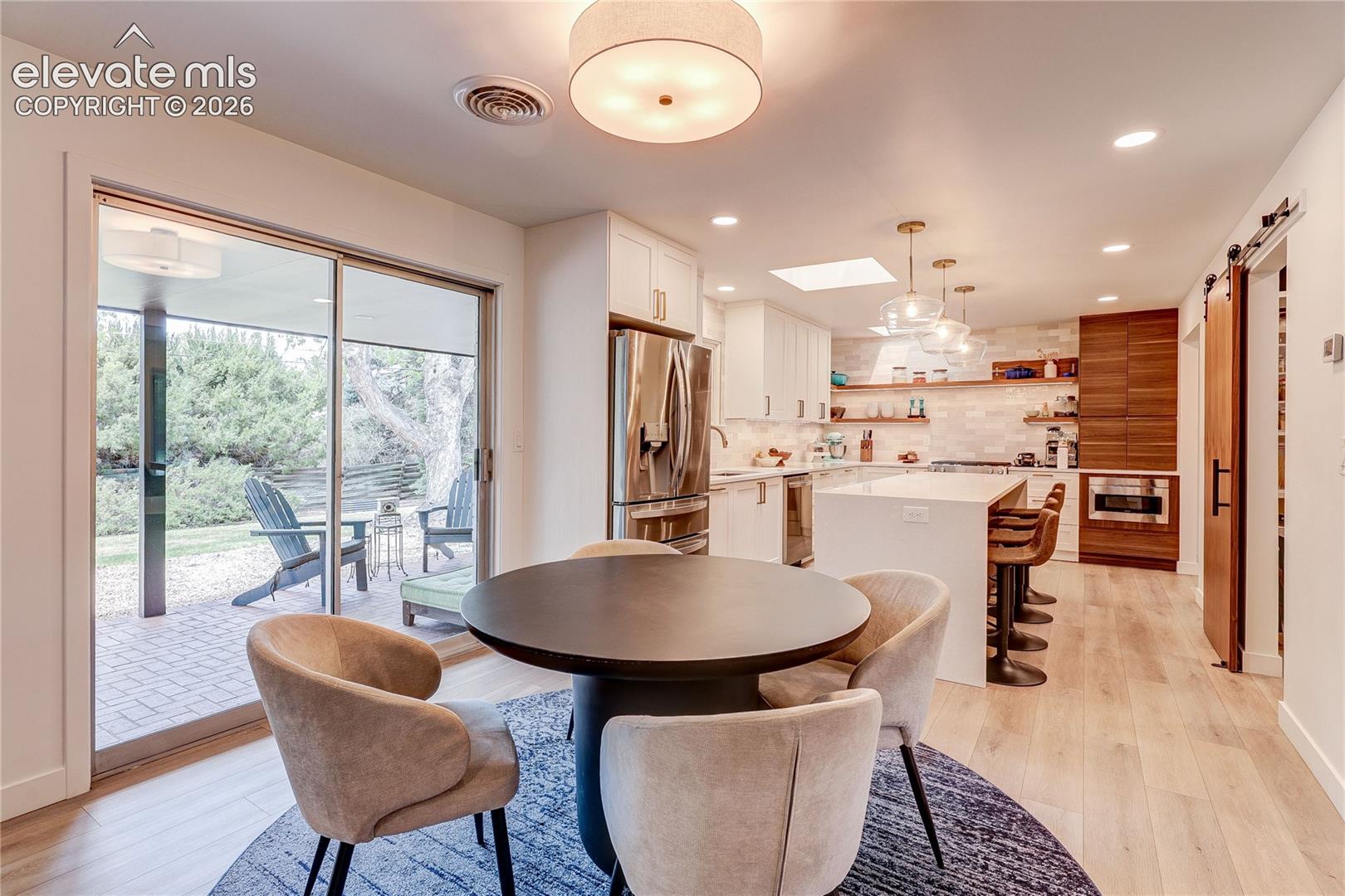 Kitchen with light wood-finish flooring, white cabinetry, a large center island, stainless steel appliances, and a skylight