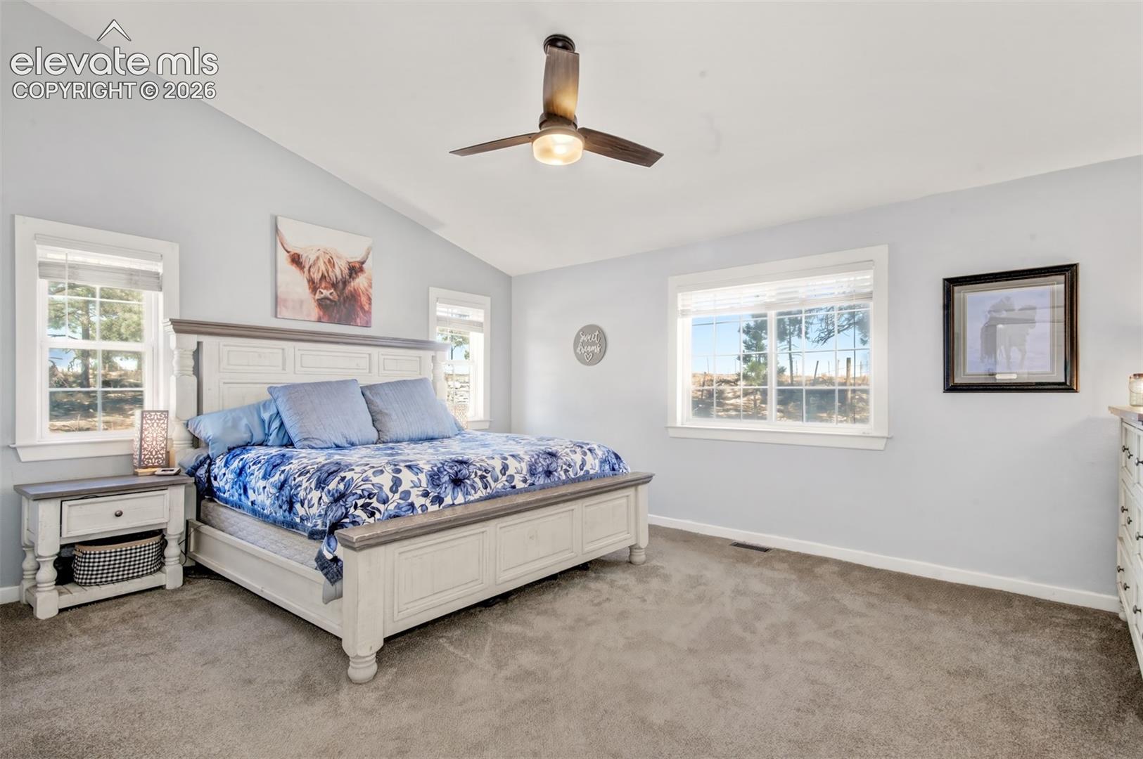 Bedroom featuring a vaulted ceiling, neutral wall coloring, carpeted flooring, large windows, and an integrated ceiling fan with a central light fixture