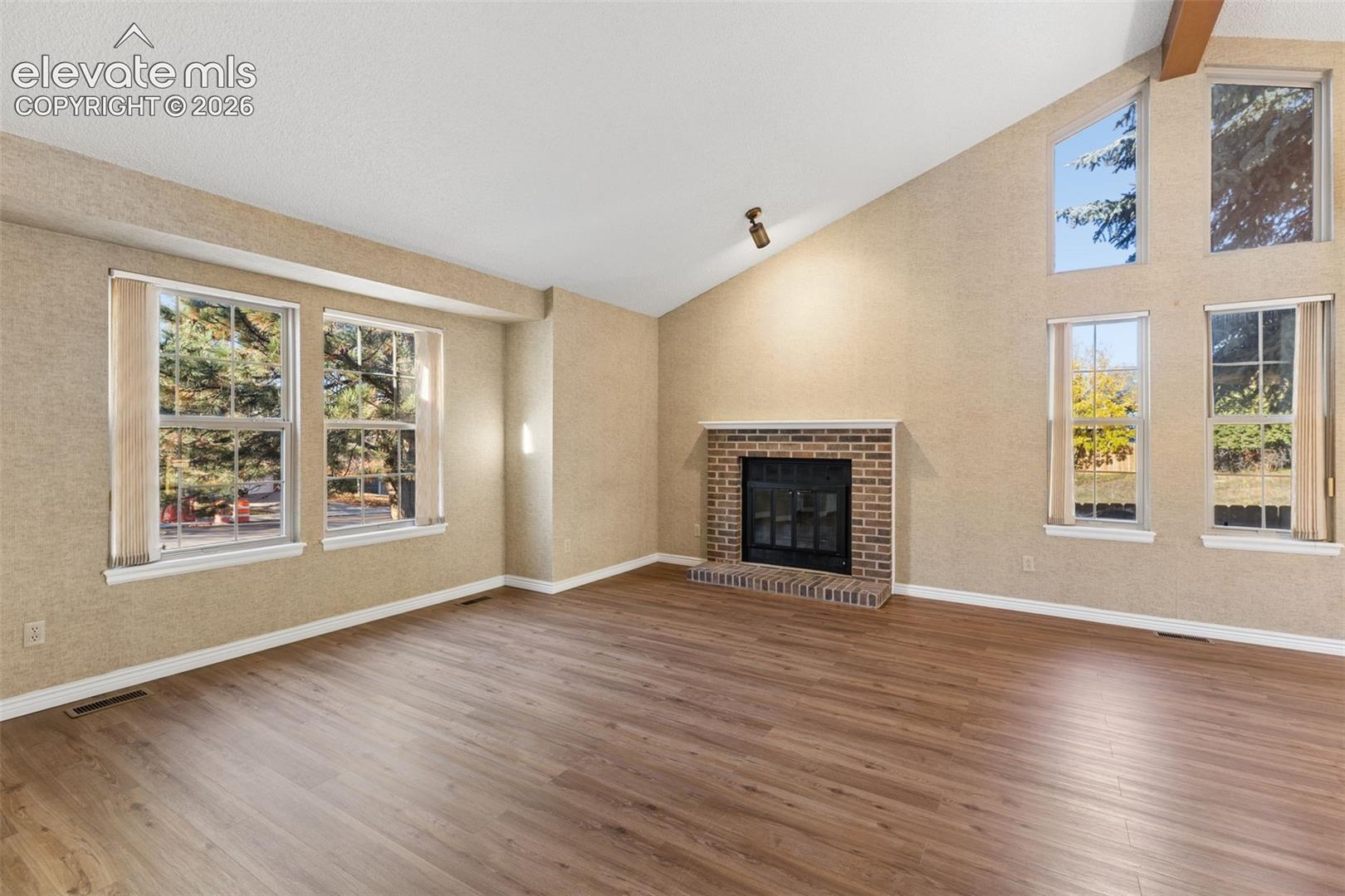 Vaulted ceilings, wood-finish flooring, brick-faced fireplace, and expansive windows