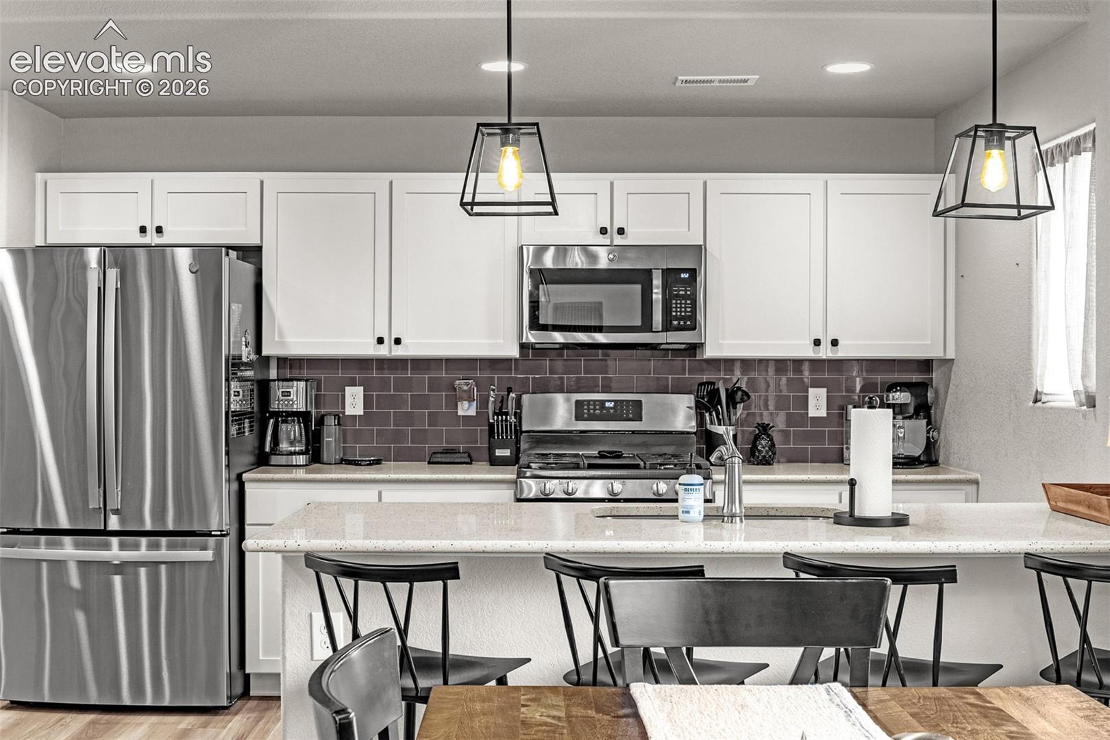 Contemporary kitchen featuring stainless steel appliances, white shaker cabinetry, a tiled backsplash, a light-toned countertop, and modern pendant lighting
