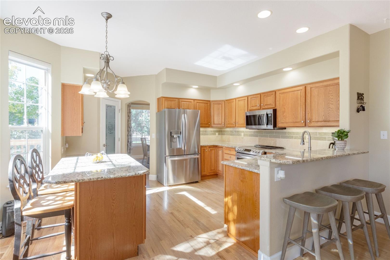 Kitchen featuring wood-finish flooring, a stone-surface island, light wood cabinetry, stainless steel appliances, and recessed lighting