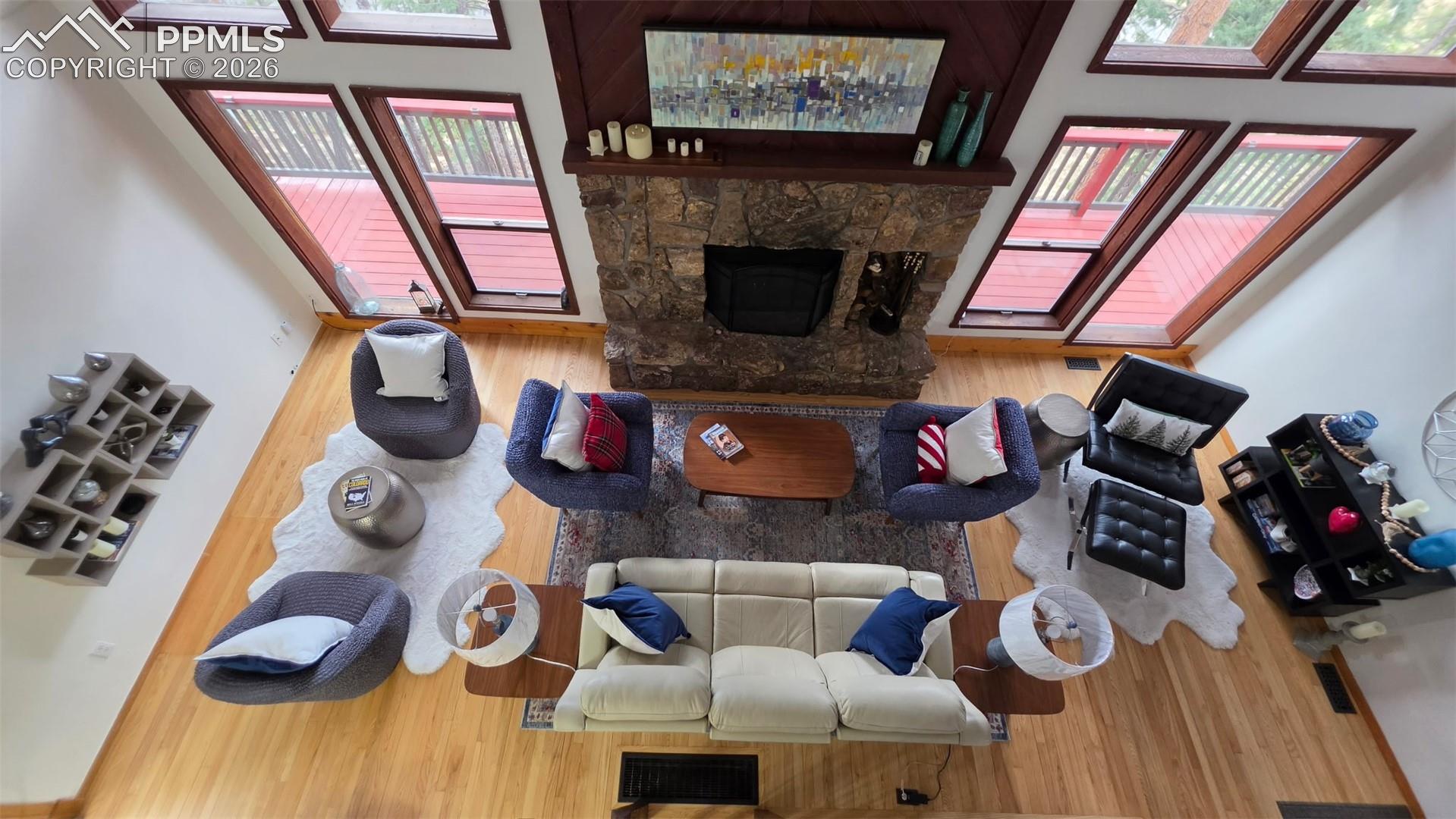 Vaulted ceiling living area featuring wood-finish flooring, a stone-clad fireplace, and prominent high windows